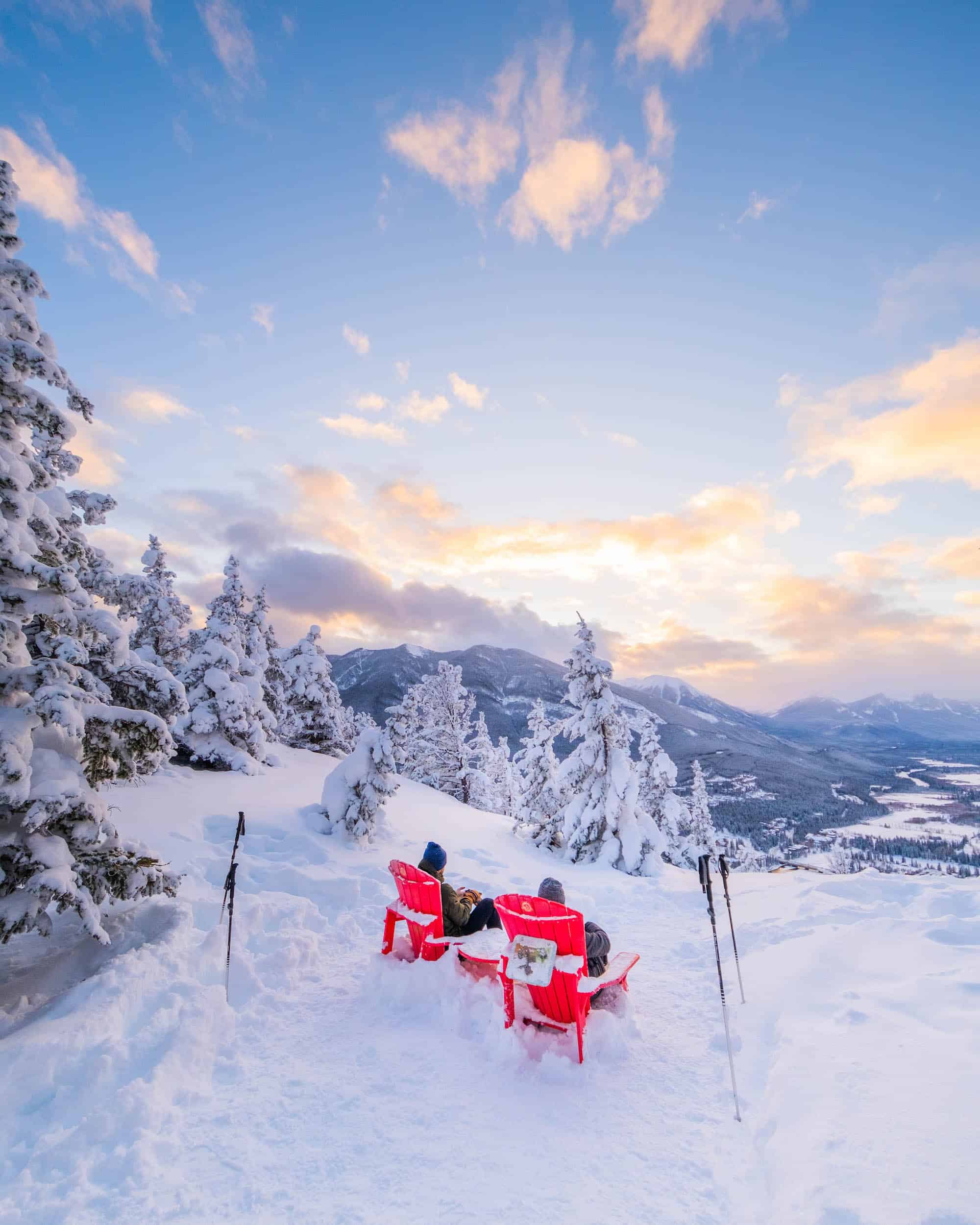 Two hikers sit in Parks Canada red chairs on summit of Tunnel Mountain