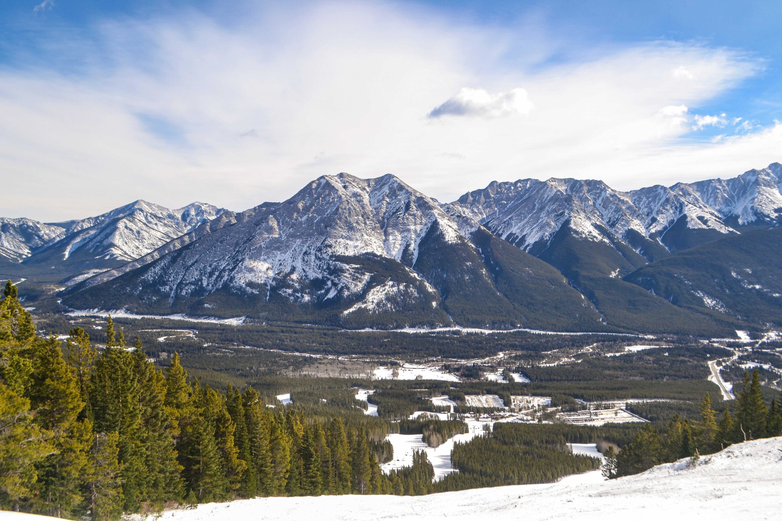 The view from mid-mountain at Kananaskis Ski Resort, looking out over a mountain range with the ski runs below