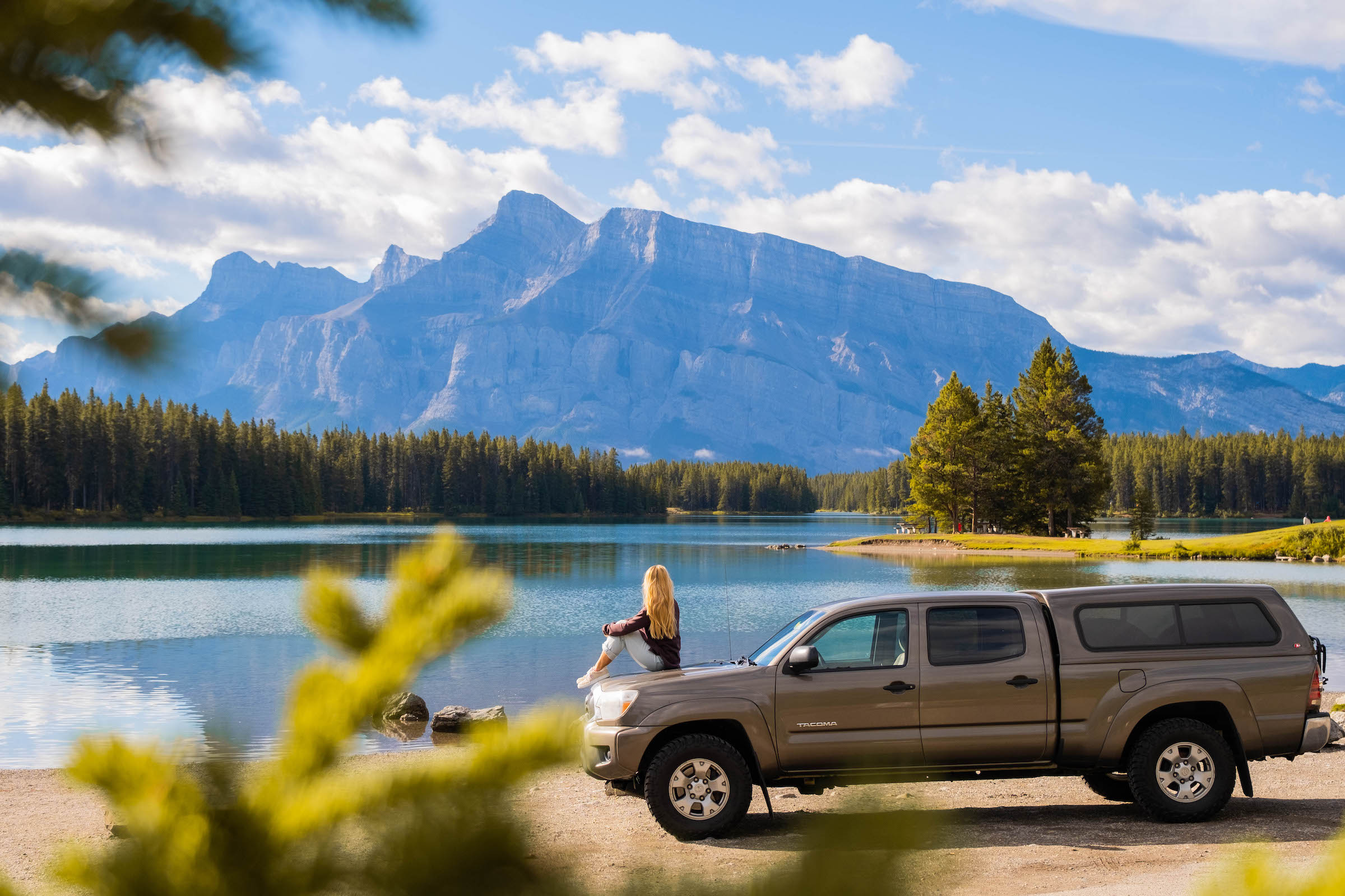 Natasha Sits On Truck At Carpark Along Lakeshore Of Two Jack Lake